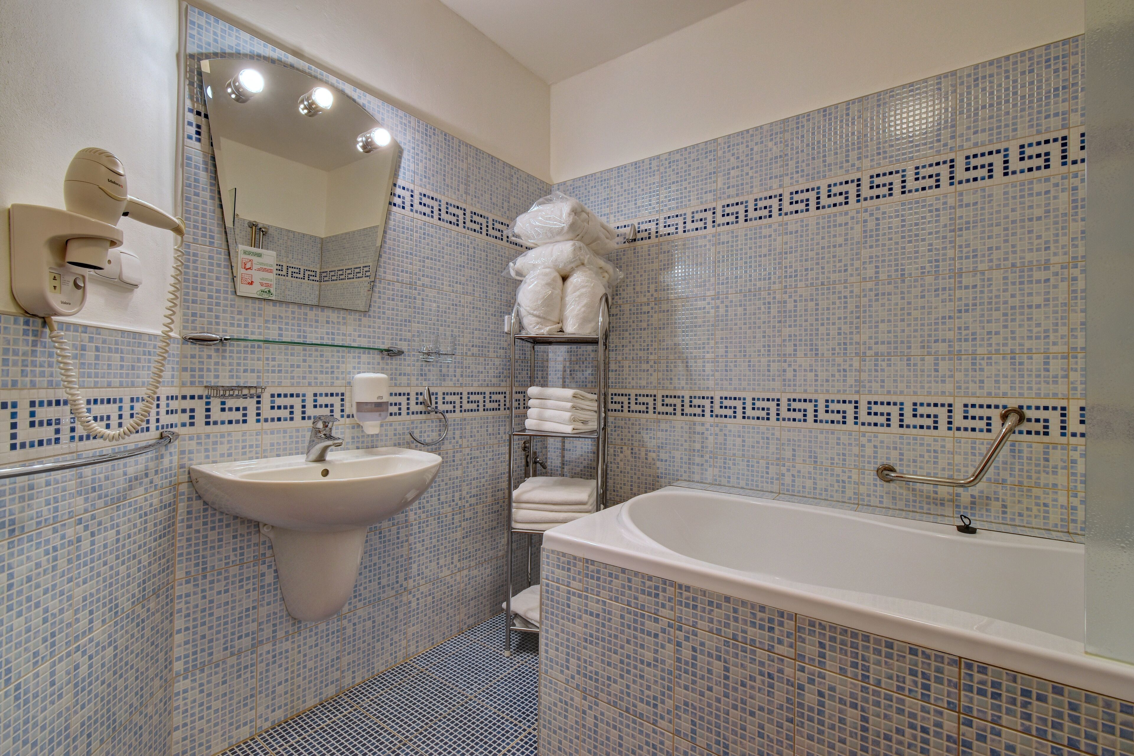 A bathroom with a sink, mirror, and bathtub. There are towels and toiletries on shelves.