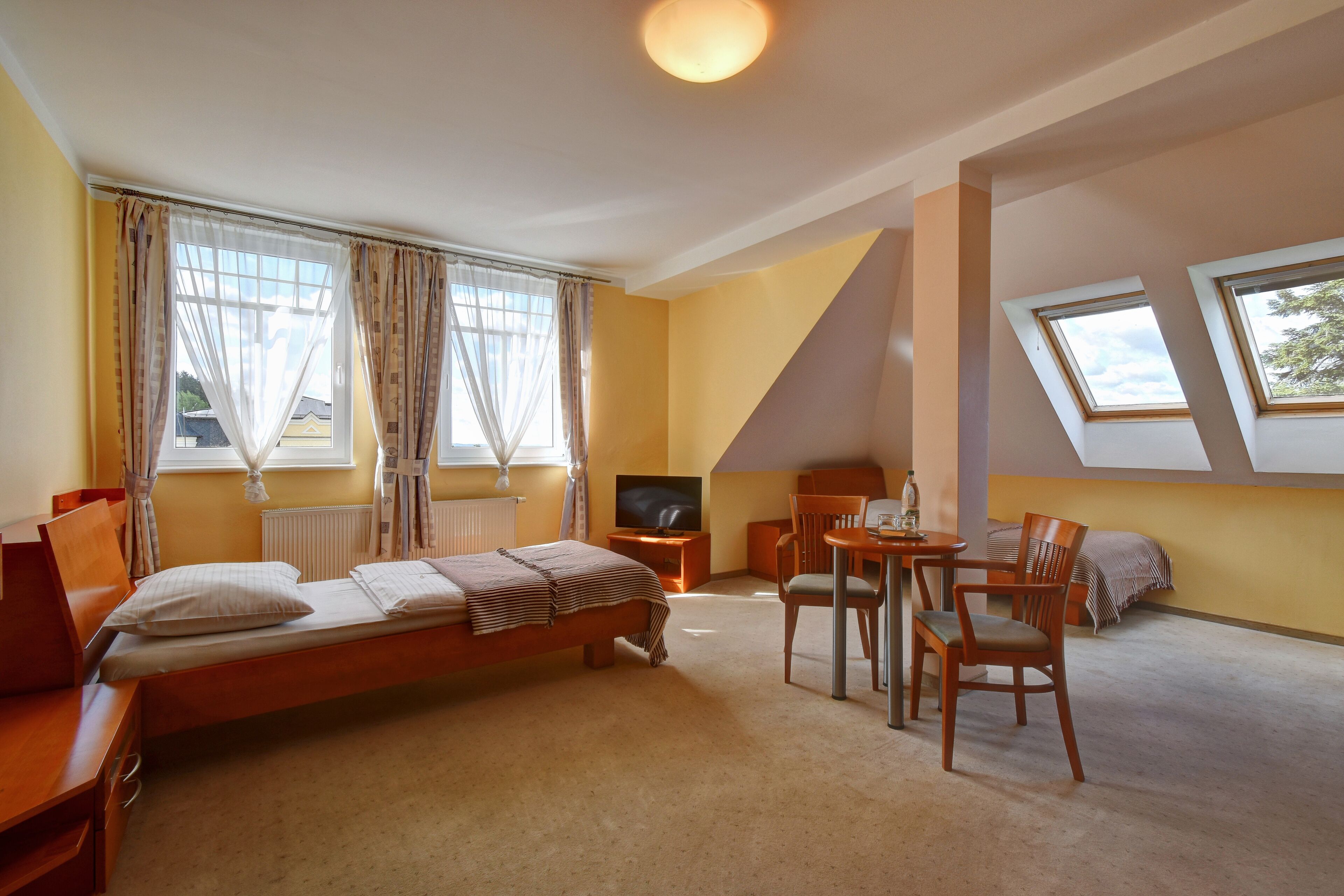 A bedroom with a bed, a desk, a chair, a TV, and skylights.