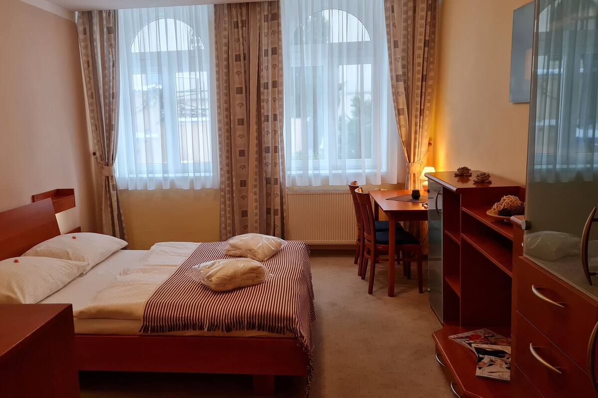A hotel room with a bed, a desk, a chair, a television, and a window with curtains.