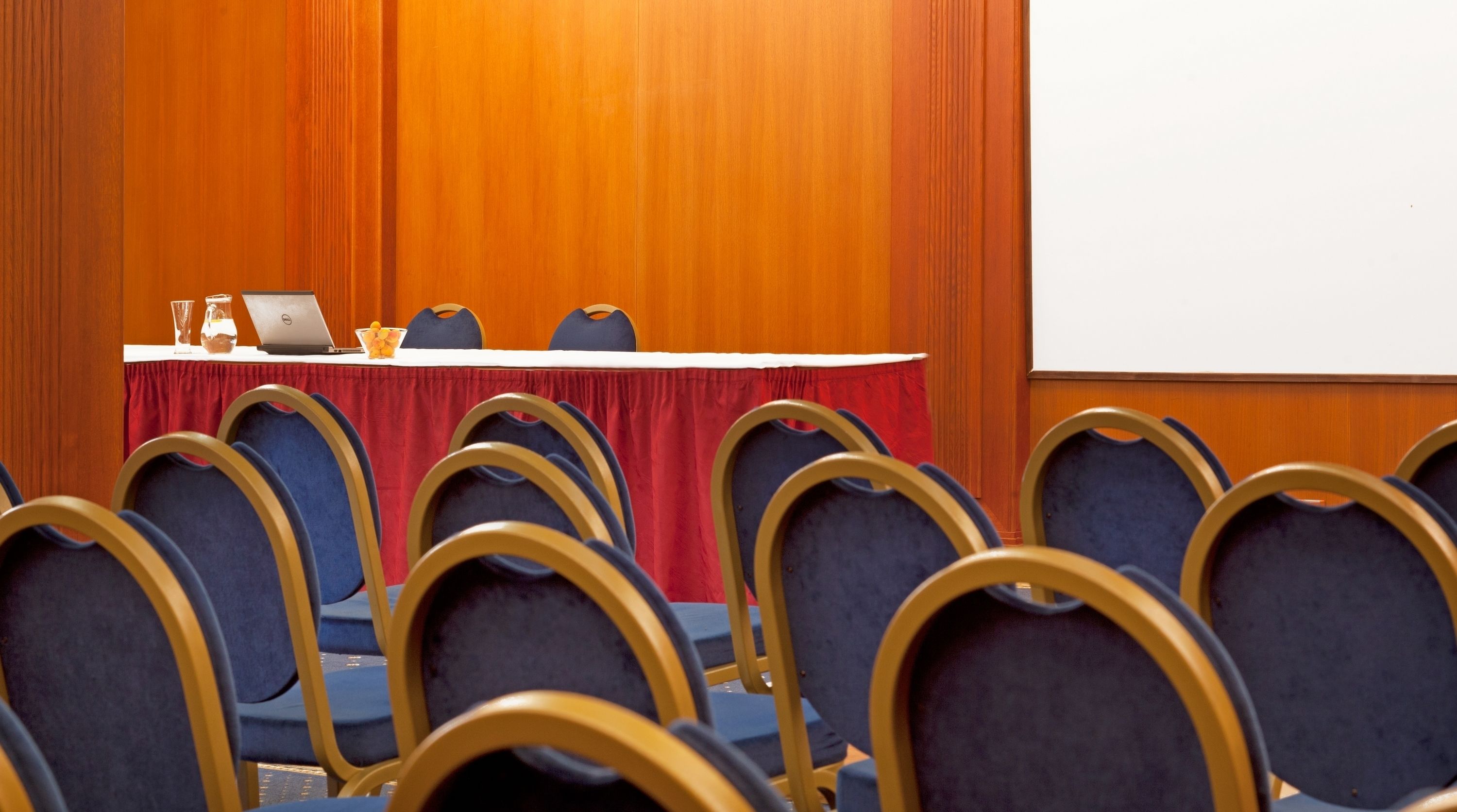 Een vergaderzaal met een ronde tafel, stoelen en een projectiescherm.