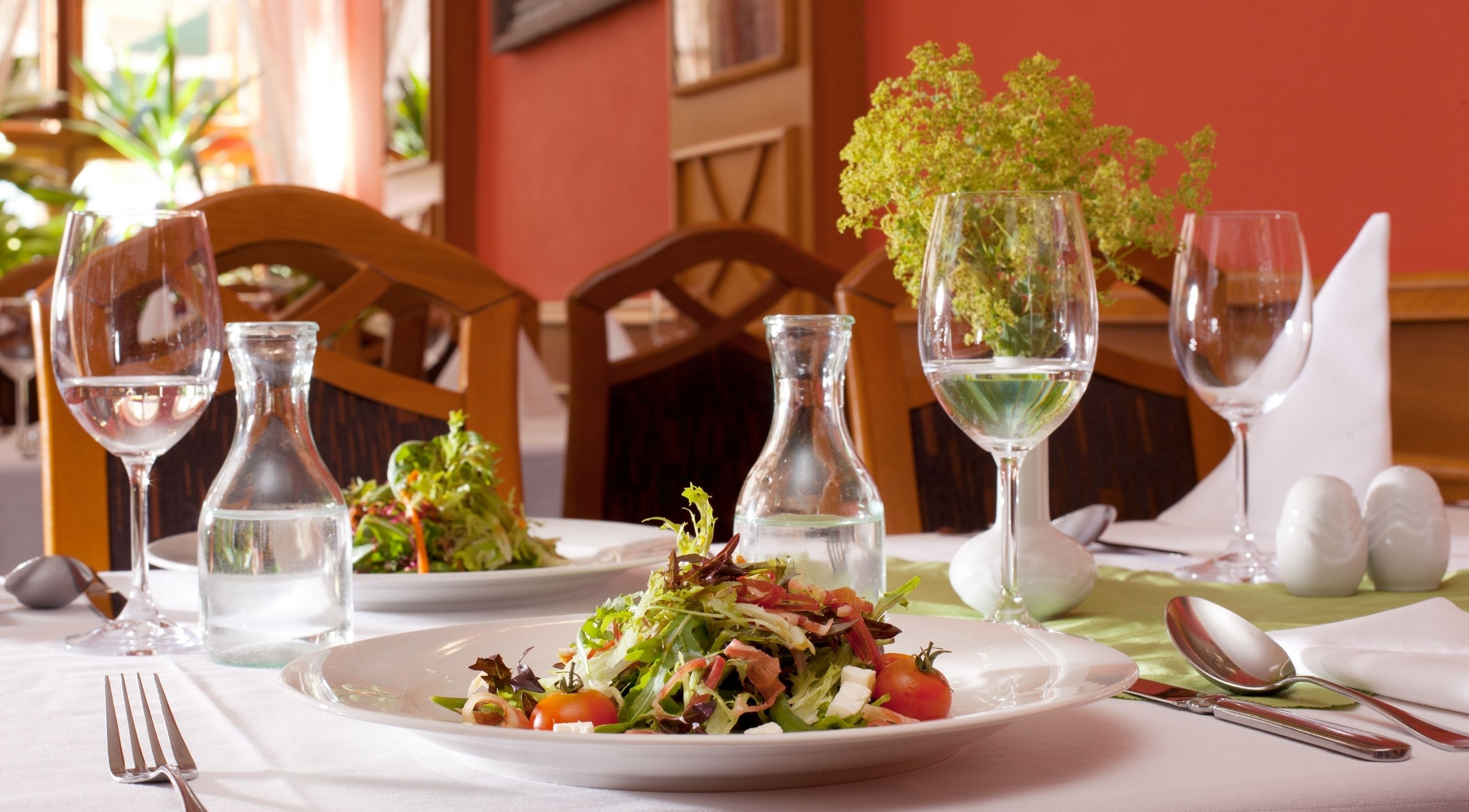 A dining table set with plates of salad, wine glasses, and cutlery.