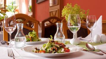 A dining table set with plates of salad, wine glasses, and cutlery.