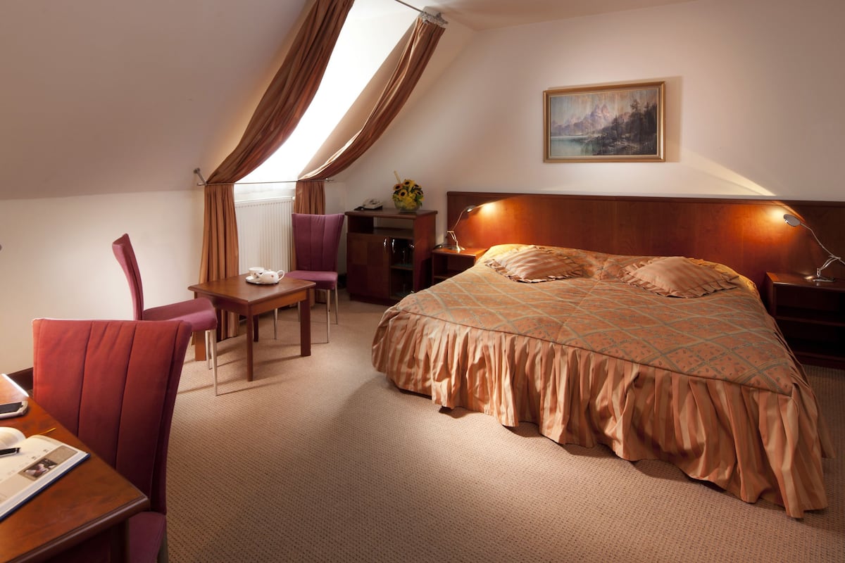 Una habitación de hotel con una cama, un escritorio con lámpara, una silla y una pequeña mesa con un jarrón de flores.