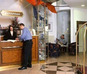 Un espace d'accueil comprenant un comptoir de réception, une signalétique indiquant la réception et une personne assise à l'arrière-plan.