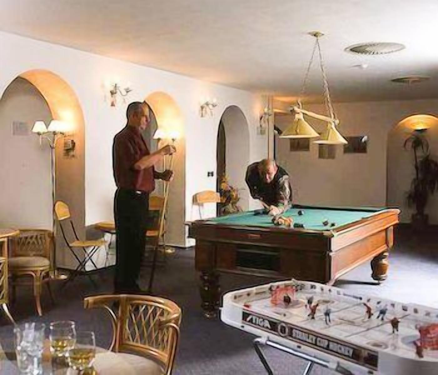 A billiards room with a pool table, a foosball table, and two people playing.