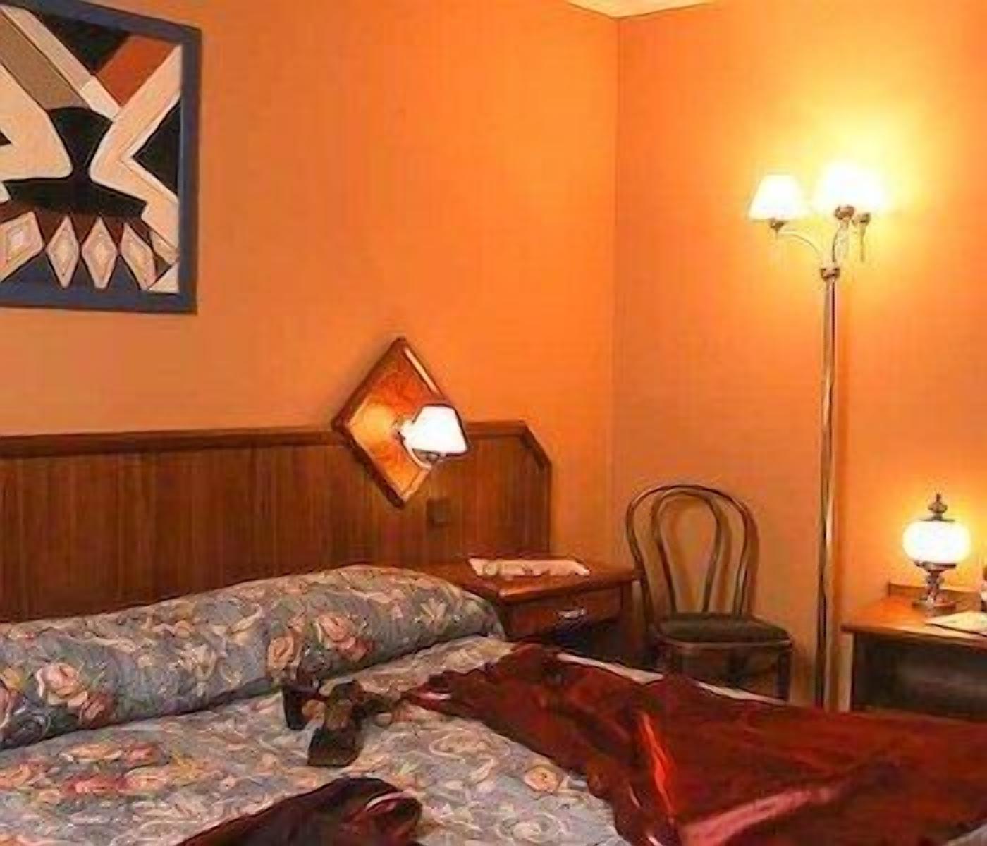 Una habitación de hotel con una cama, una mesita de noche, una silla y una lámpara de pie.