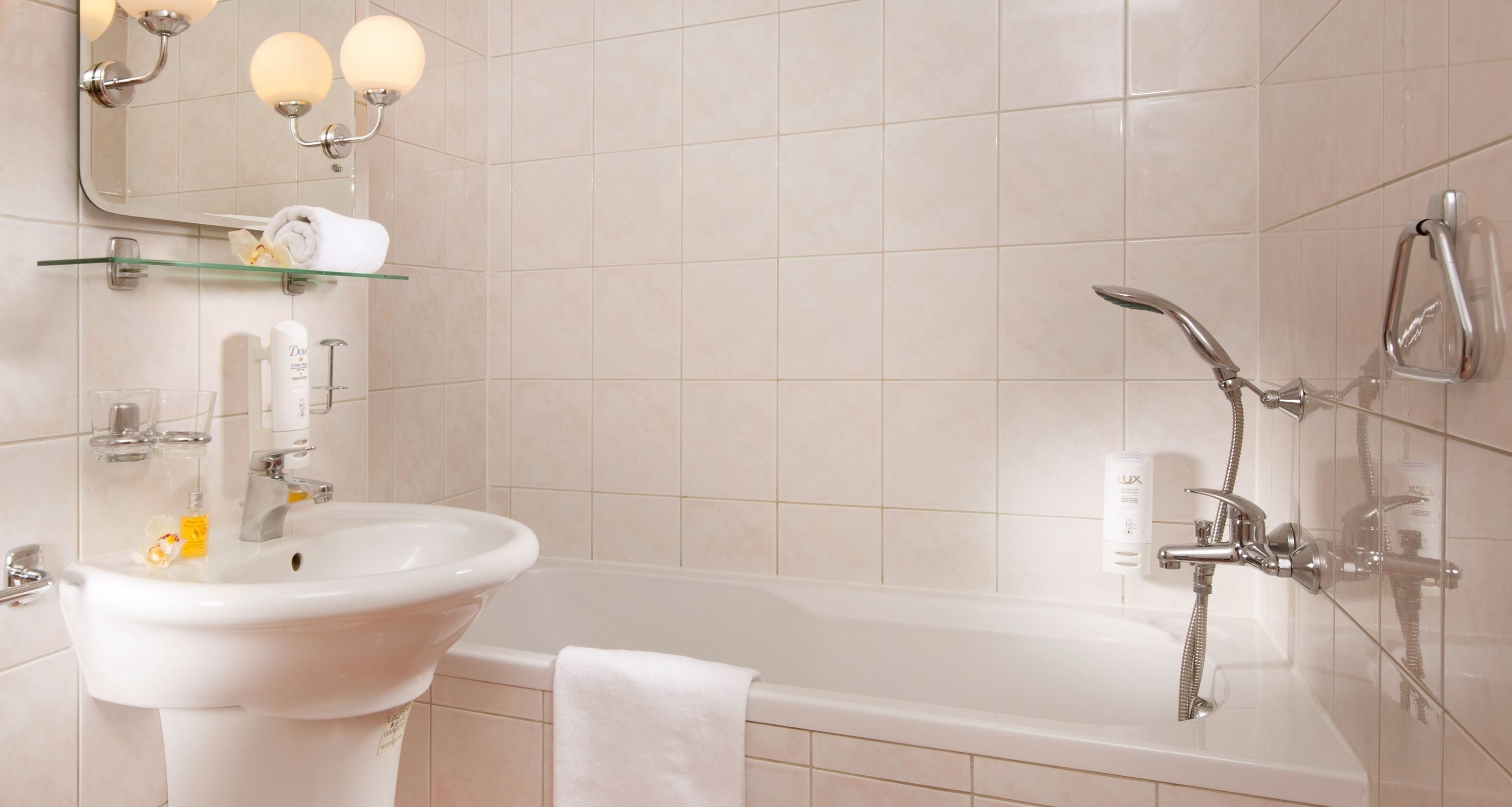 A modern bathroom with a white sink, glass shelf, and a bathtub with a showerhead.