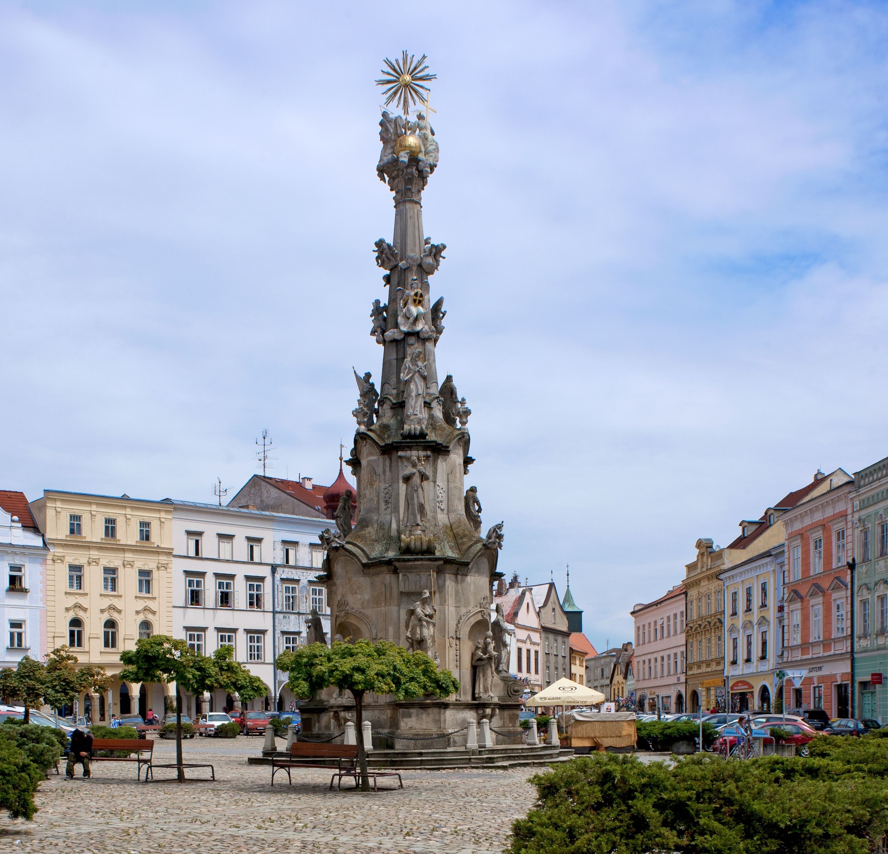 Ein historisches Denkmal mit aufwendigen Skulpturen, umgeben von Kopfsteinpflaster und klassischer europäischer Architektur.