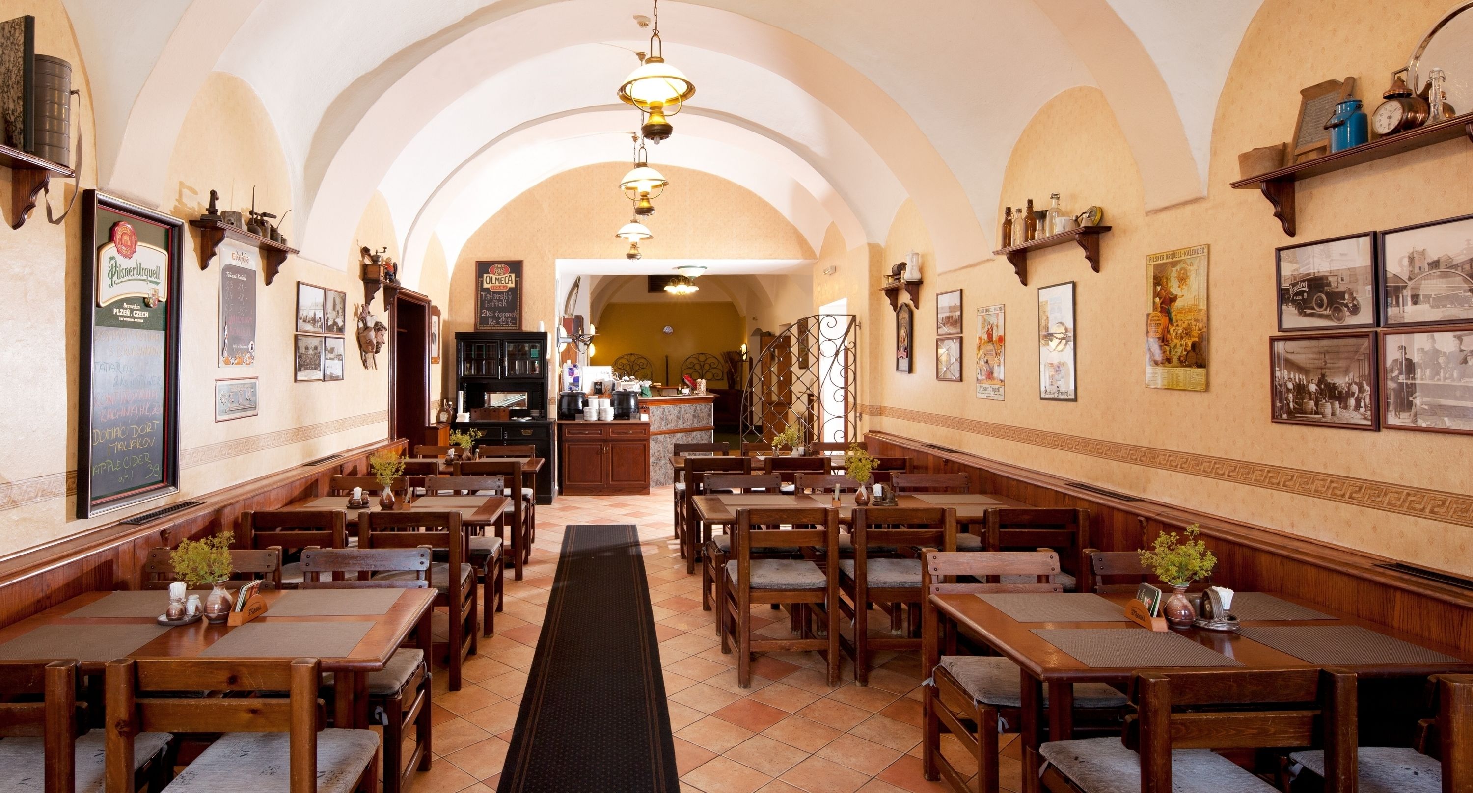 Un restaurante con mesas y sillas de madera, un tapete negro que lleva a la barra, y varias fotos y letreros enmarcados en las paredes.