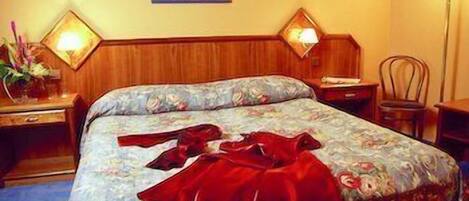 A hotel room with a bed, a nightstand, a lamp, and a wall decoration.