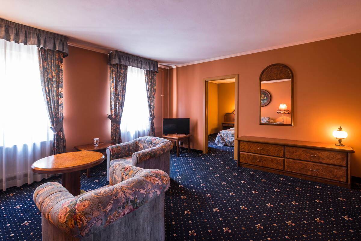 Una habitación de hotel con sofá, una mesita, televisión, cómoda y espejo.