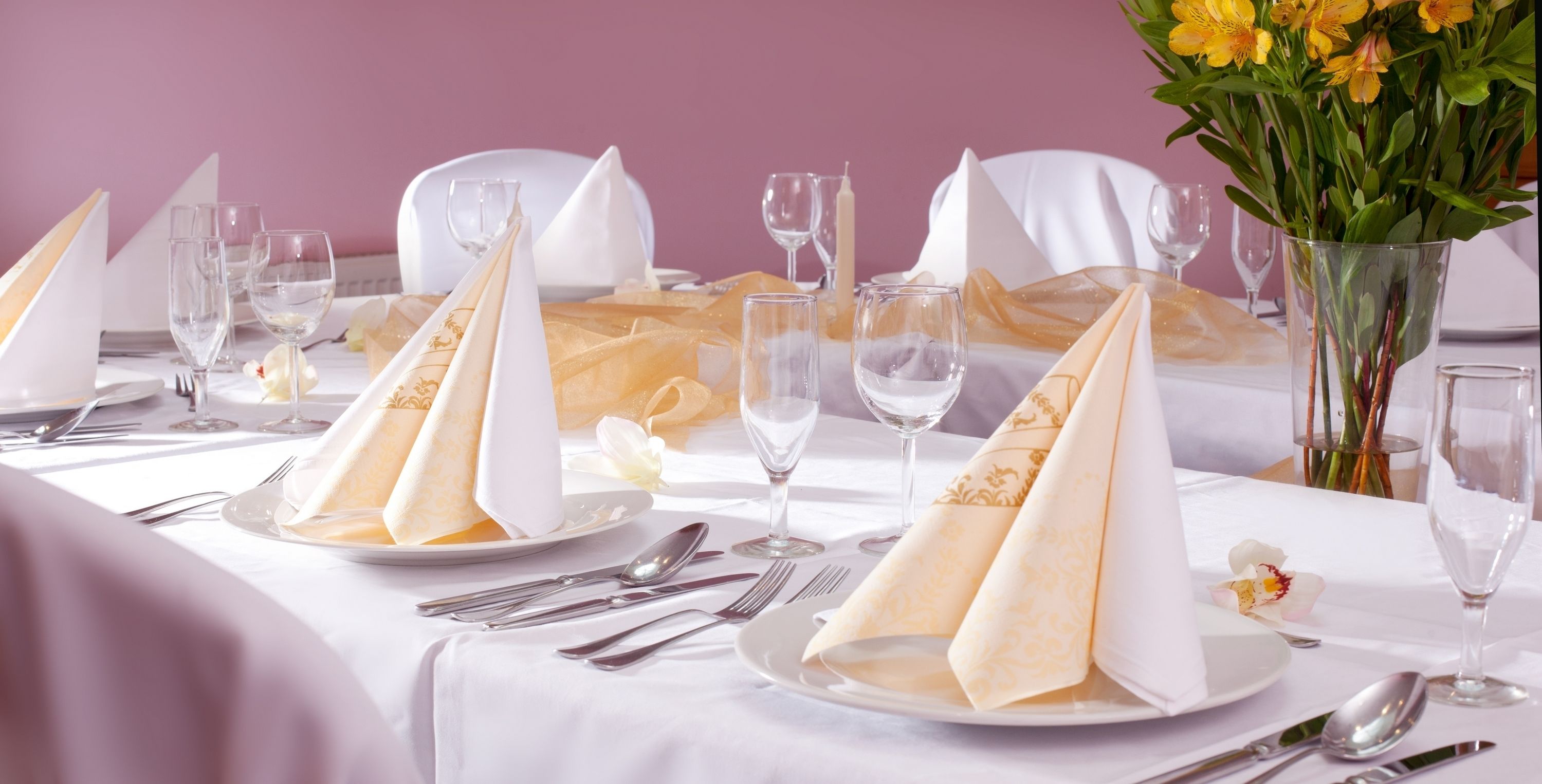 Une table dressée pour un repas formel, avec des nappes blanches, des serviettes pliées et de la verrerie transparente.