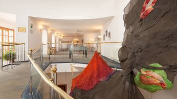 A hotel lobby with a glass railing, a staircase, and a large tapestry on the wall.