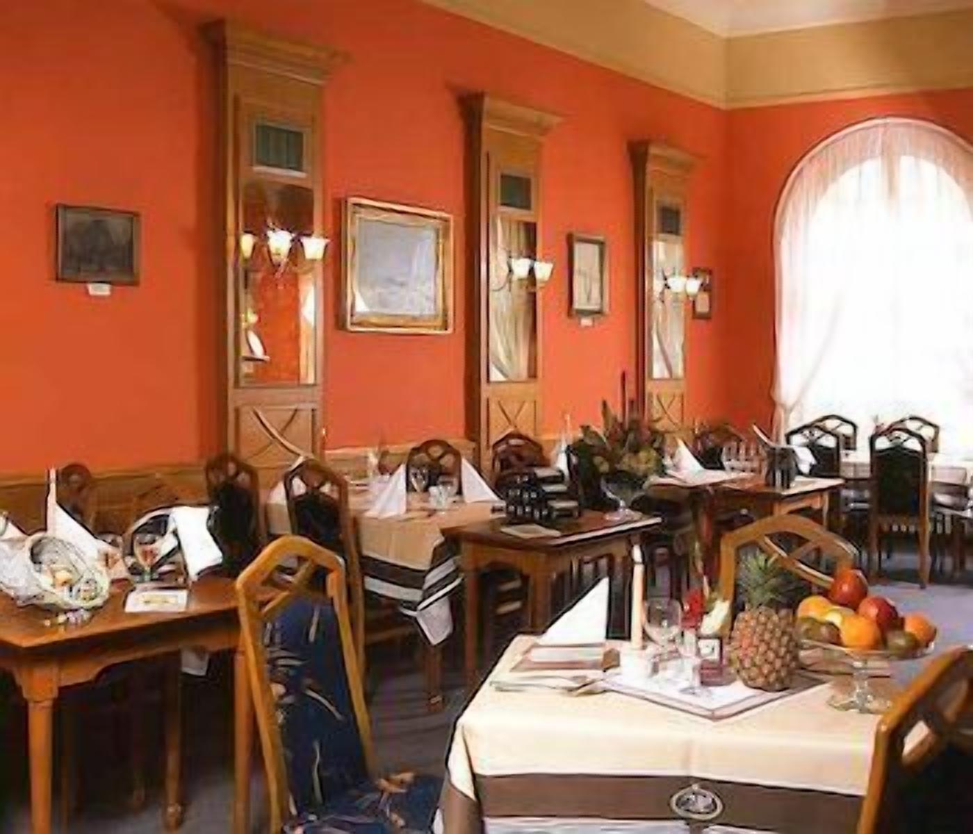 A dining area with wooden tables and chairs, a fruit basket on one table, and framed pictures on the walls.