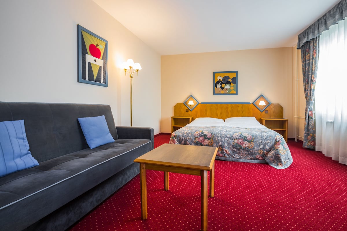 Una habitación de hotel con un sofá, una cama con ropa de cama floral, una mesa de madera y dos lámparas de noche.