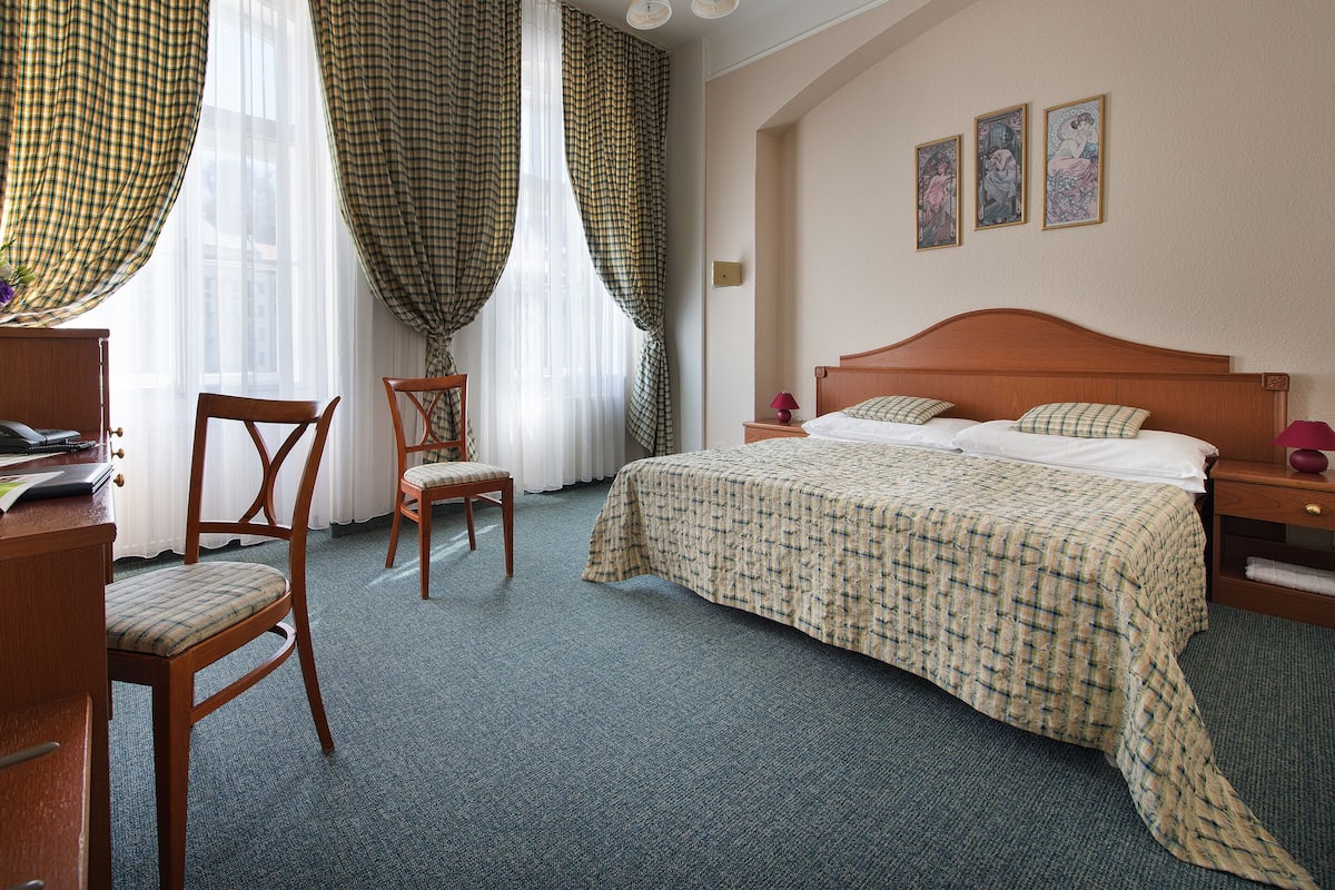 A hotel room with a bed, a chair, a desk, and a nightstand.