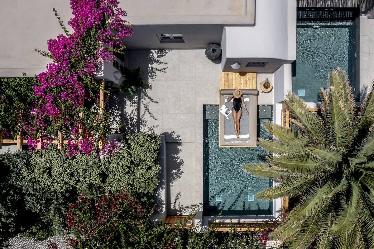 An aerial view of a hotel with a swimming pool, lush greenery, and a wooden deck.