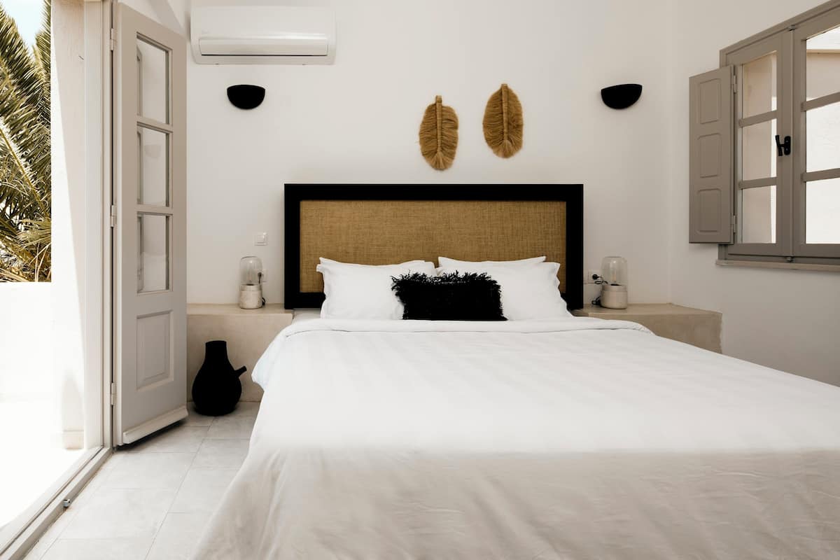 Une chambre à coucher avec un lit, des tables de chevet, un climatiseur fixé au mur et une fenêtre dont les volets sont ouverts.
