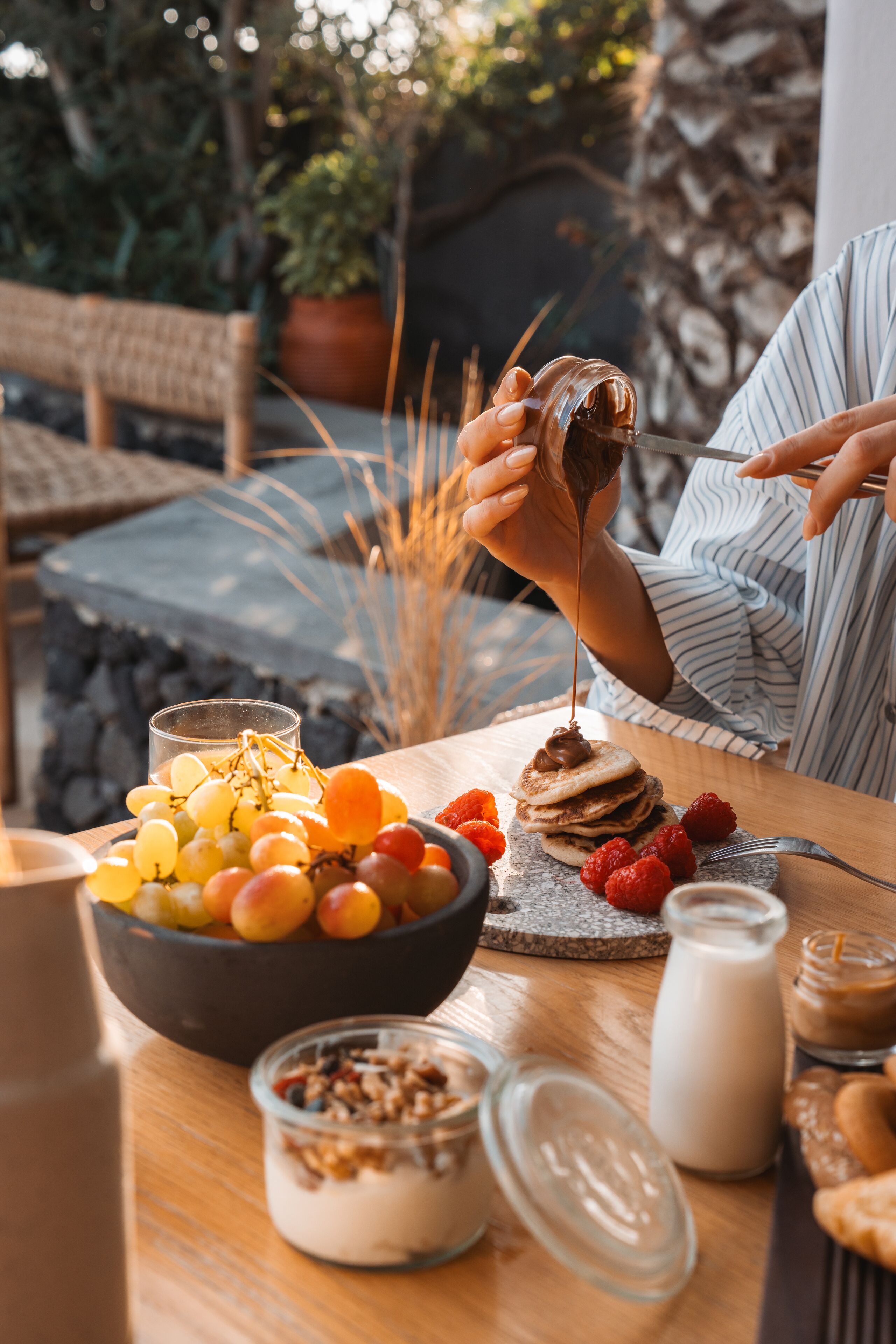 Une table mise pour le petit-déjeuner avec un bol de fruits, un verre de lait et une assiette de crêpes nappées de sirop.