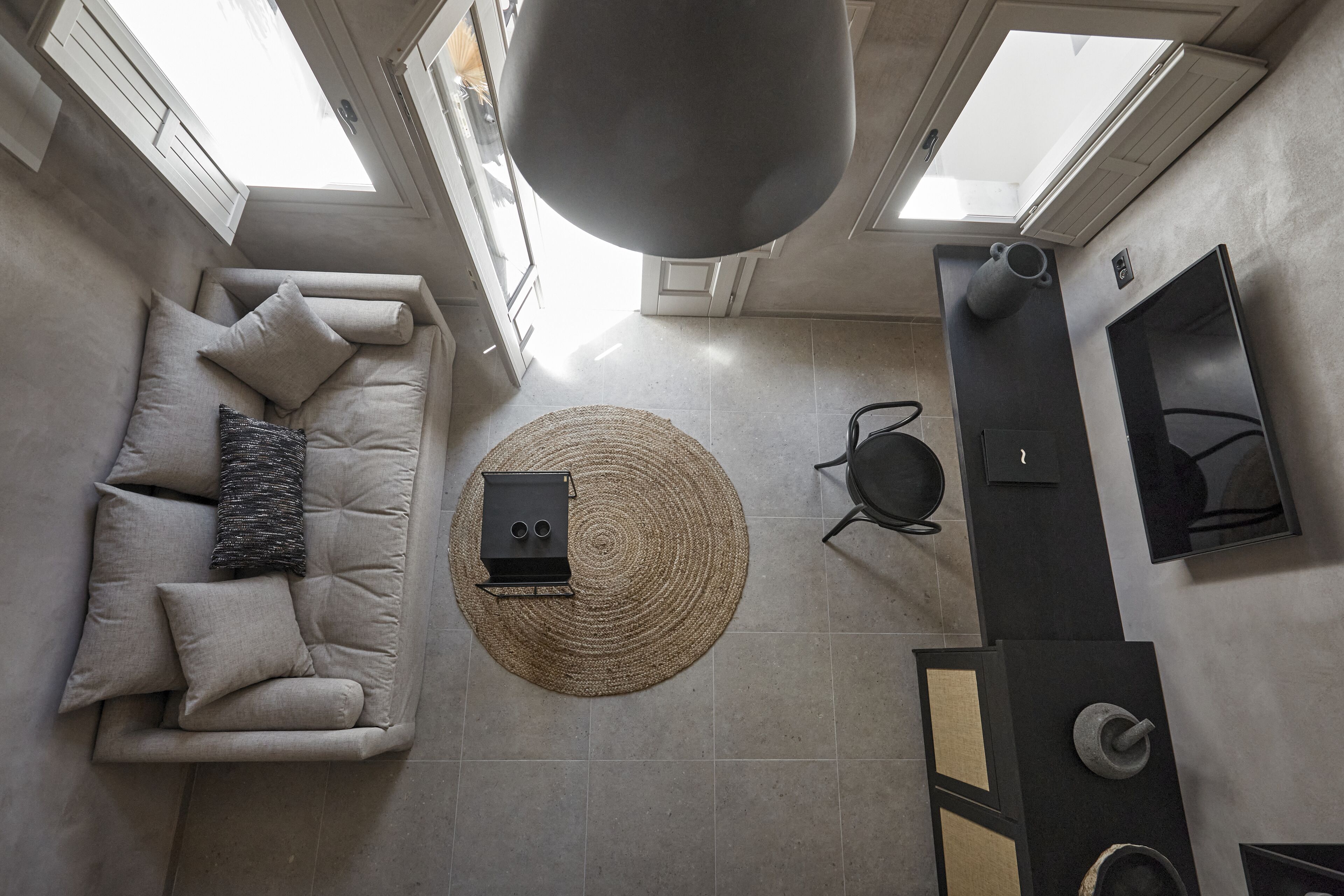 A modern living room with a sofa, a round woven rug, a black speaker, and a wall-mounted TV.