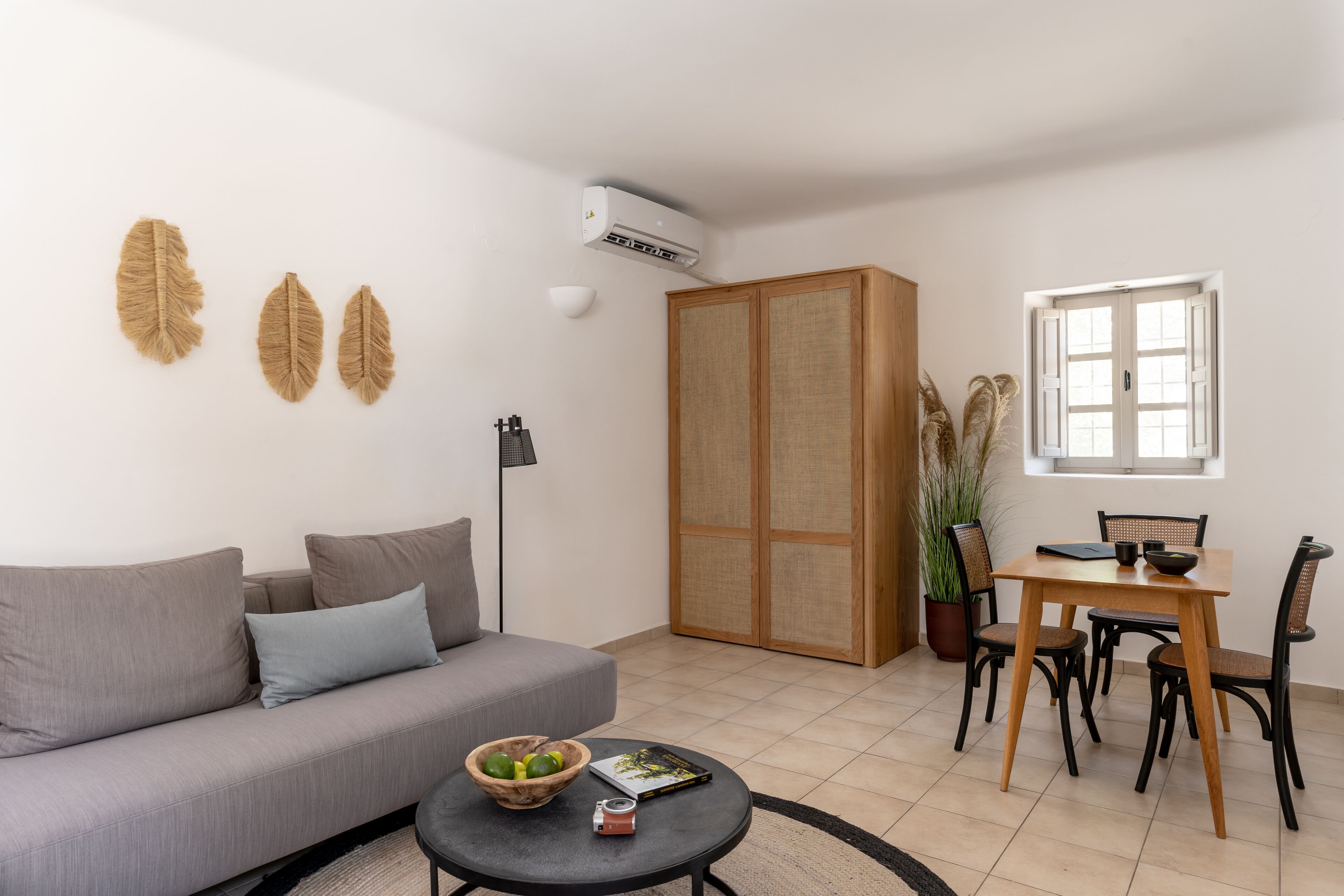 Una sala de estar con un sofá, una mesa de comedor con sillas, una mesa de centro con un cuenco y un libro, una planta en maceta y una ventana con vistas.