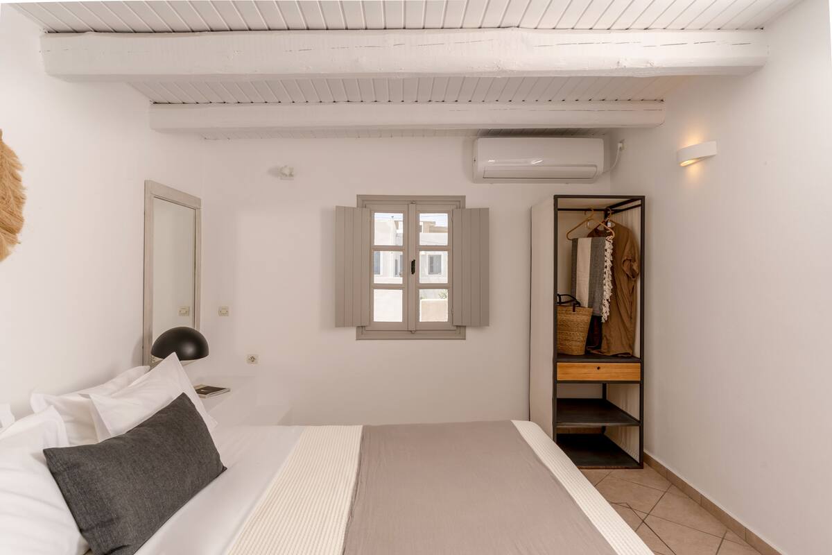 A bedroom with a bed, a wardrobe, a window, and an air conditioning unit.