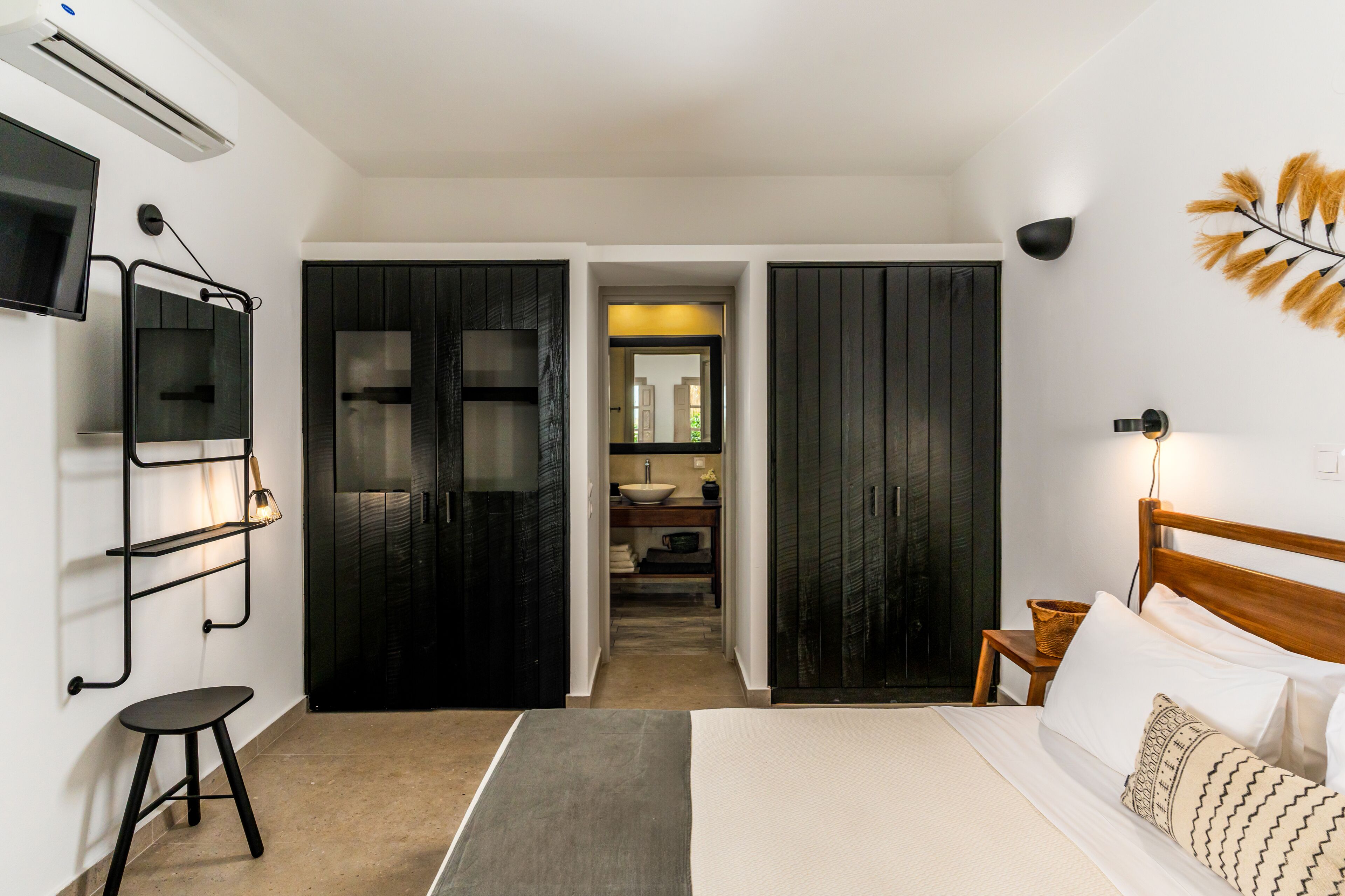 A modern bedroom with a large bed, a TV mounted on the wall, and a wardrobe with a mirror.