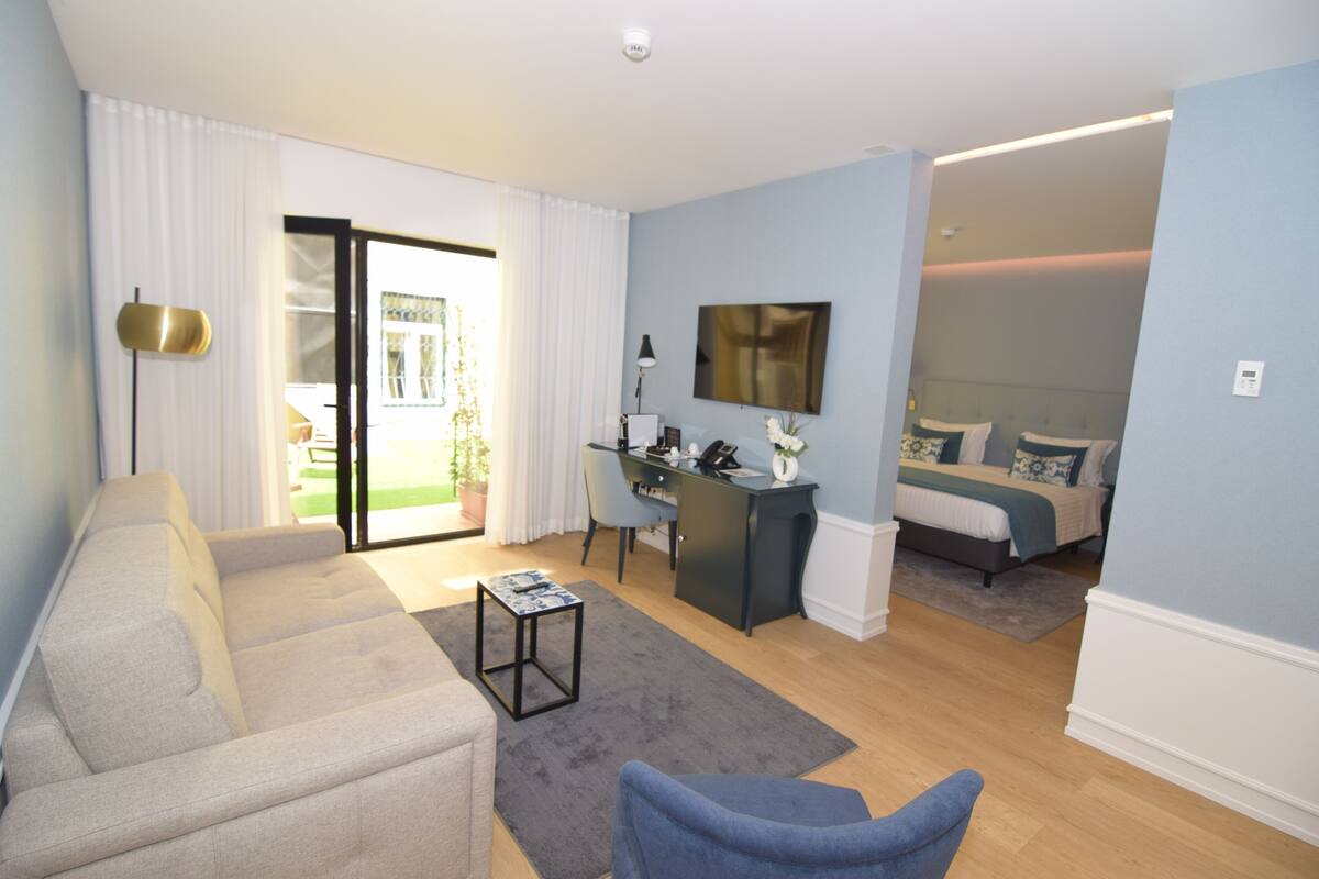 Una sala de estar moderna con un sofá, una mesita y un escritorio. Hay una cama en la habitación contigua.