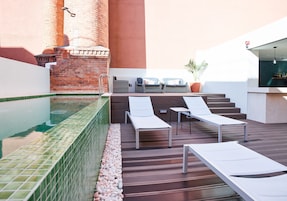 A rooftop pool area with lounge chairs, a small table, and a brick chimney.