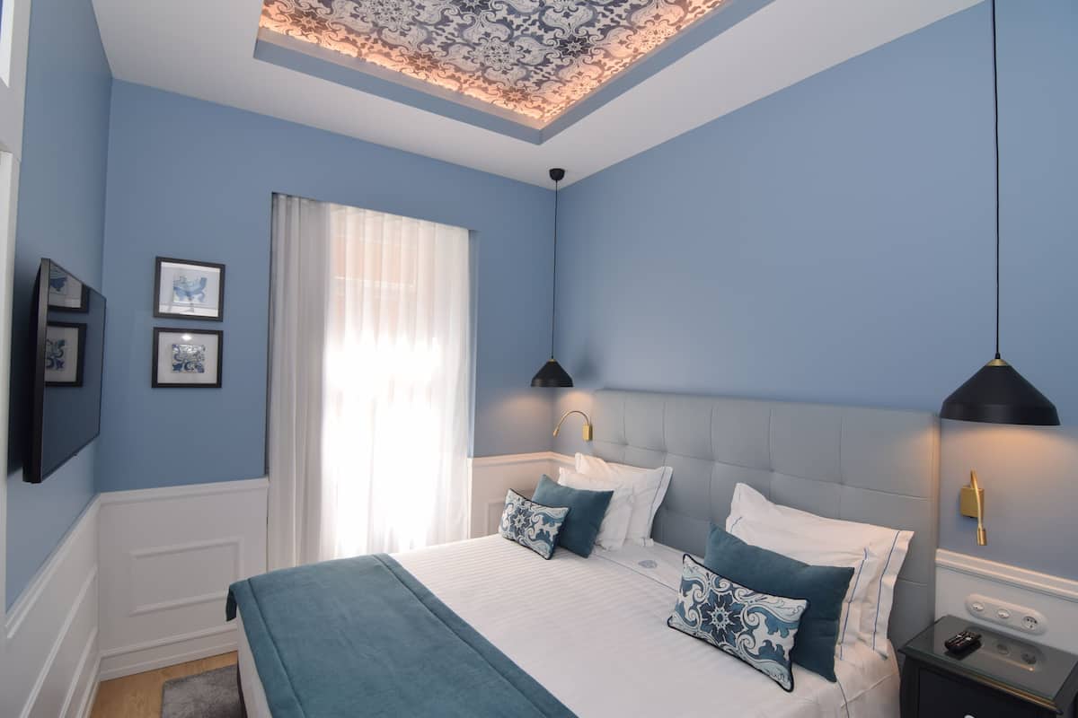 Un dormitorio con una cama grande, dos mesitas de noche, una lámpara de techo y una ventana con cortinas.