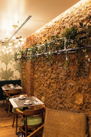 Een restaurant met bakstenen muren, houten tafels en groene fauteuils.