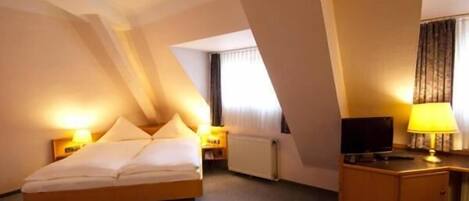 A hotel room with a bed, a desk, a television, and a lamp.