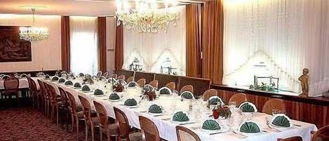 Un salón de banquetes con largas mesas dispuestas para un evento formal, con candelabros y cortinas decorativas.