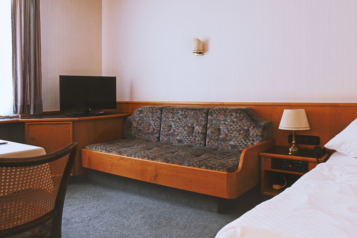 Ein Hotelzimmer mit Sofa, Fernseher, Lampe, Bett und Schreibtisch mit Stuhl.