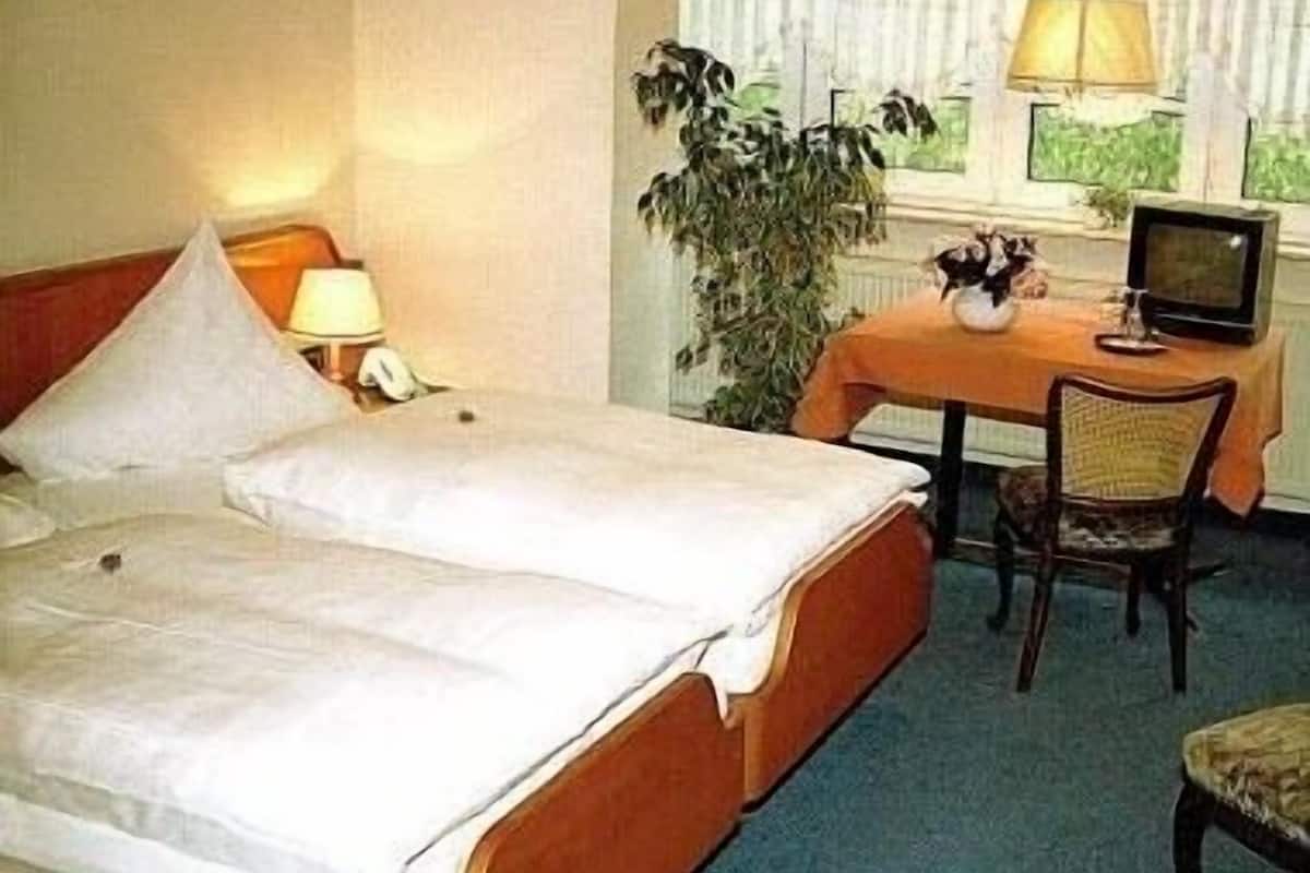 Ein Hotelzimmer mit Bett, Schreibtisch, Stuhl, Fernseher und einem fenster mit Vorhängen.