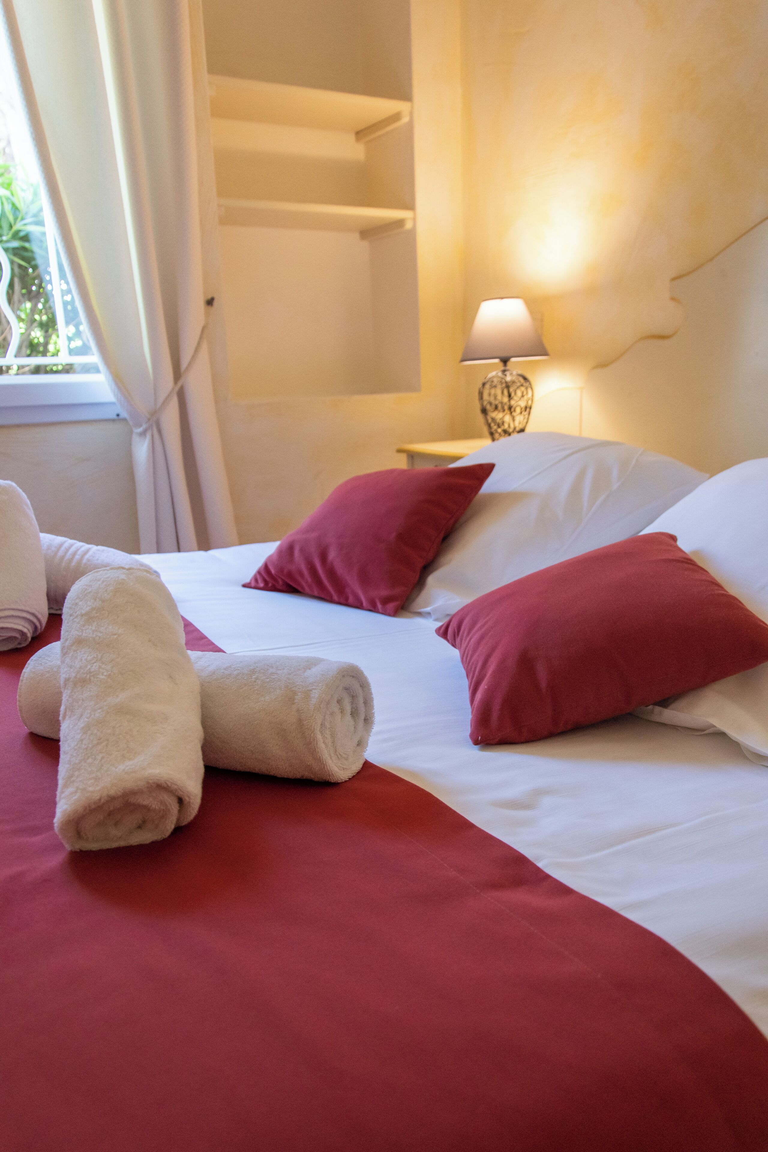Una habitación de hotel con una cama, ropa de cama roja y blanca, una lámpara y toallas.