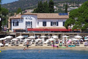 Un hotel con vista a la playa, múltiples sillas de descanso y sombrillas.