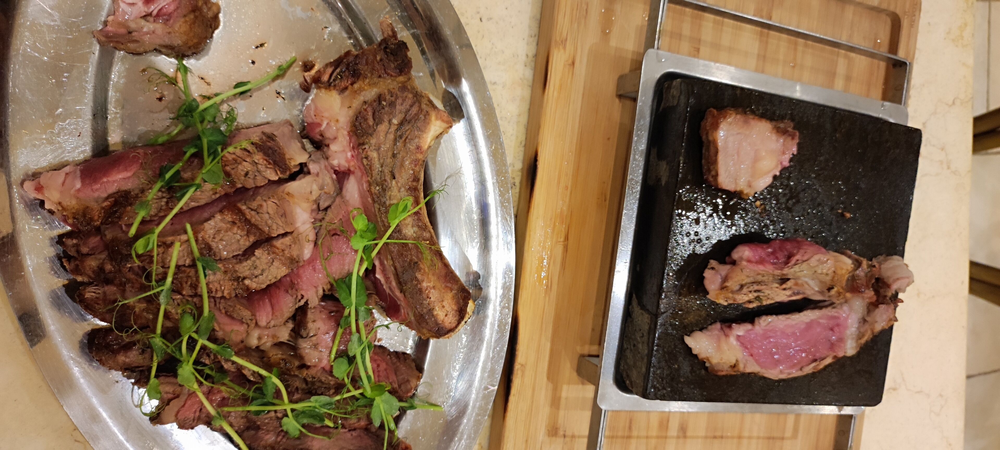 A kitchen counter with a metal tray holding sliced meat and a black cutting board with meat pieces.