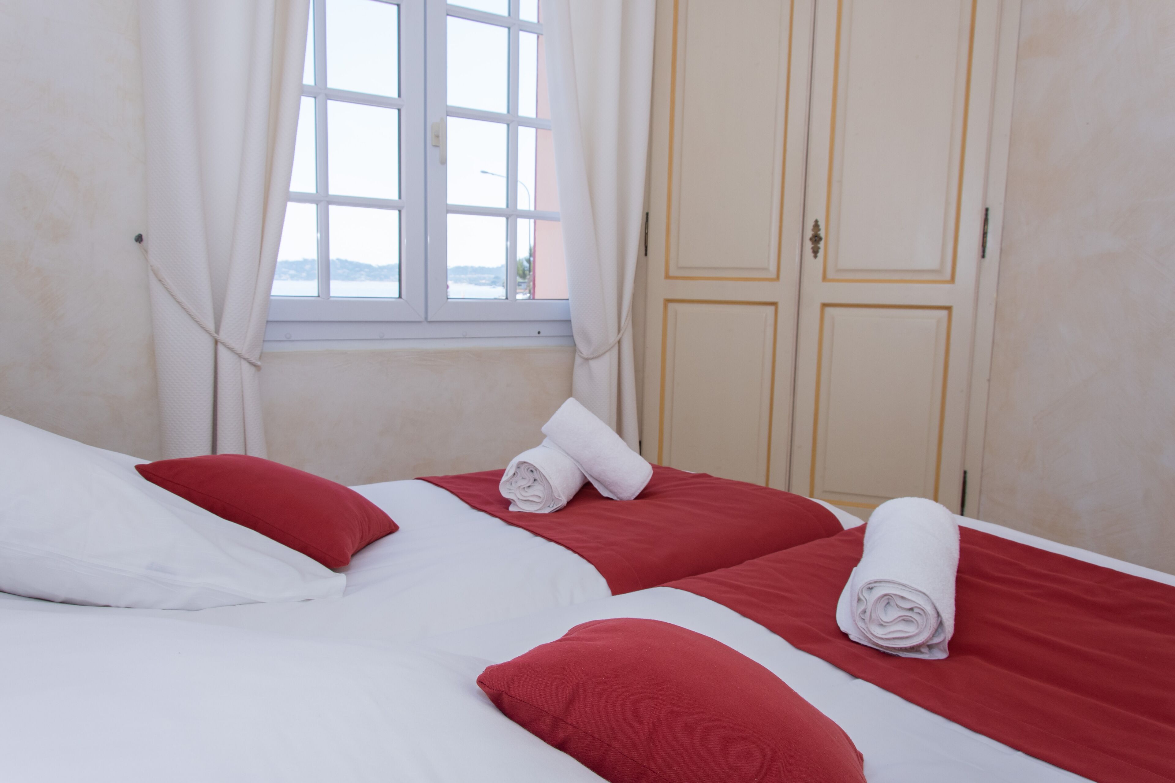 A hotel room with two beds, each with red and white bedding, and a window with curtains.
