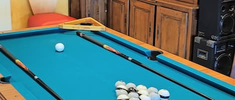 A pool table with balls, a pool cue, and a Harley-Davidson sign above it.