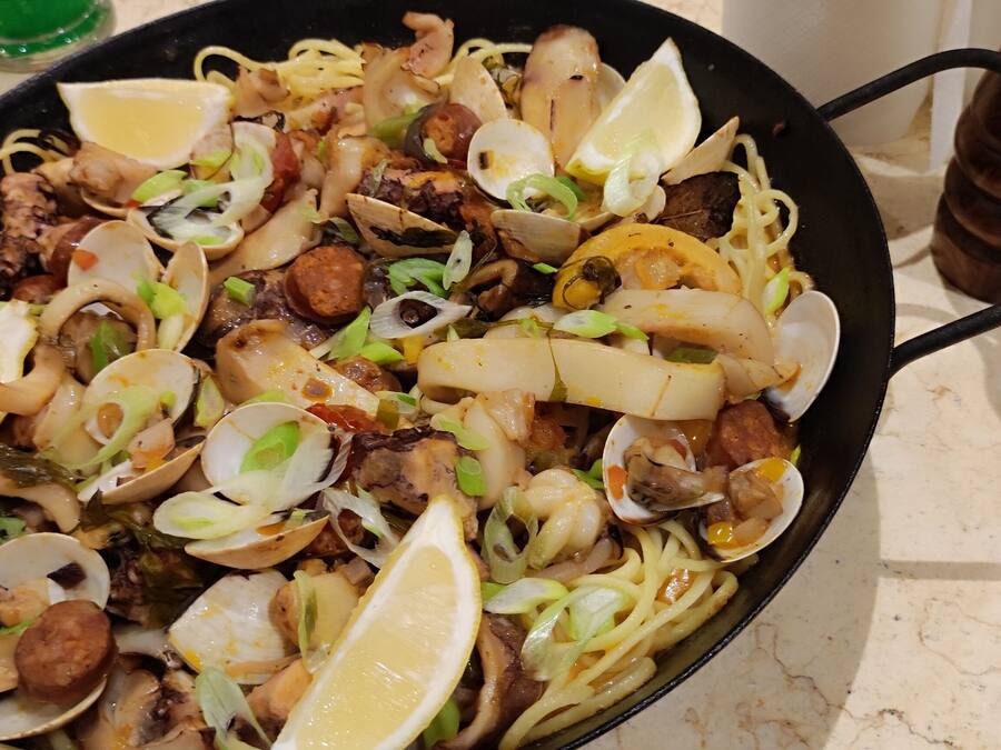 Un plat de pâtes aux fruits de mer, garni de rondelles de citron et d’oignons verts.