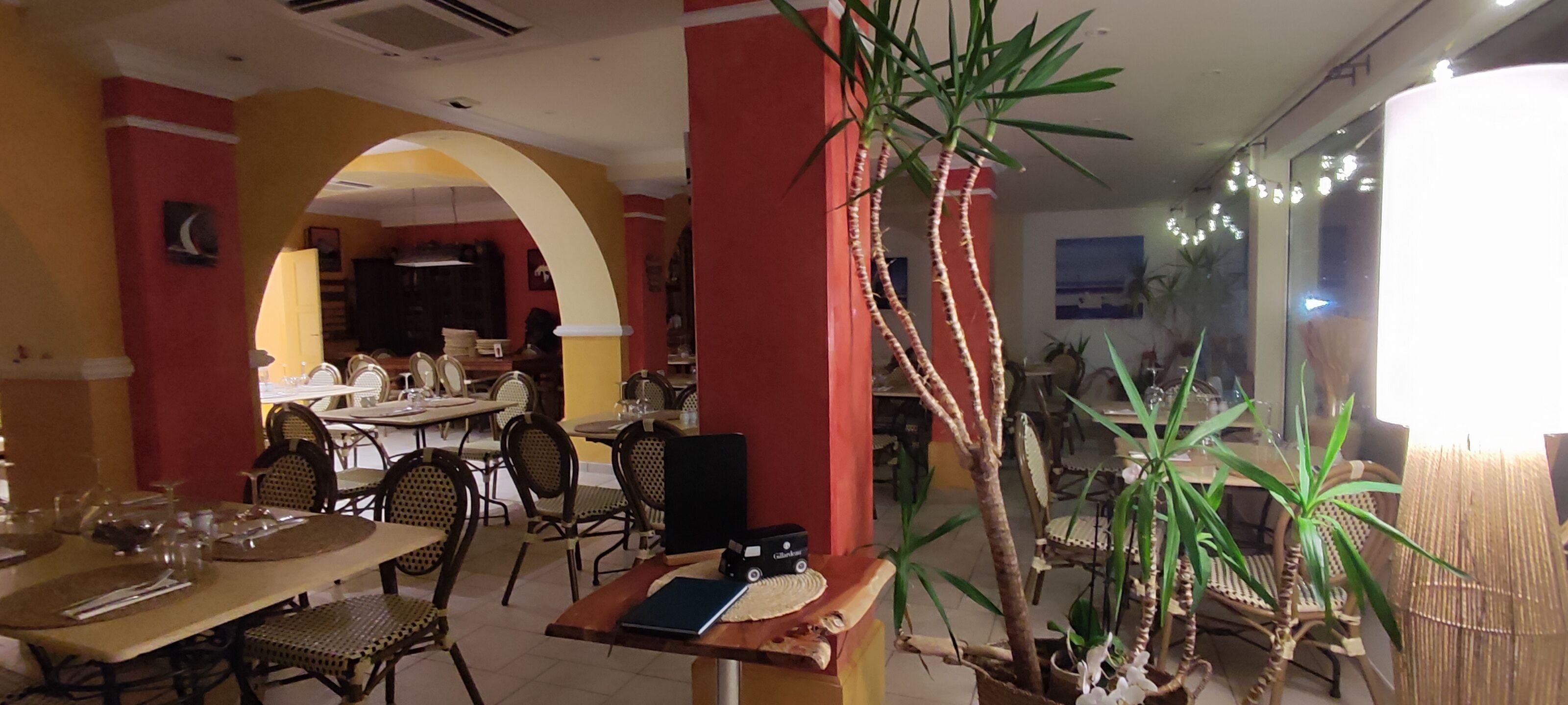 A restaurant with tables and chairs, a plant, and a wall with a picture.