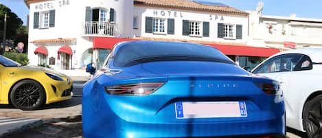 A blue car parked in front of a hotel with a red awning and a sign that reads "HOTEL SPA".