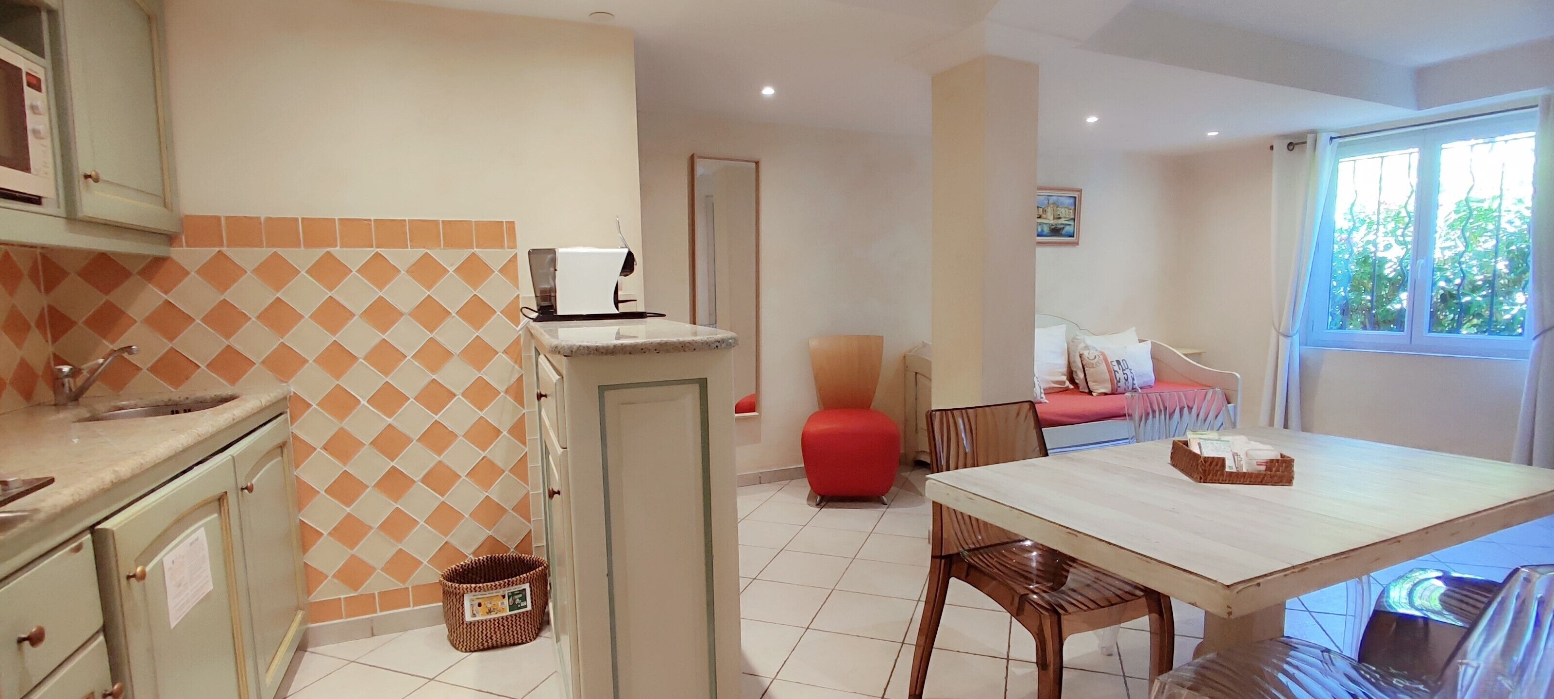 Una cocina con microondas, cafetera y lavamanos. Hay una zona de comedor con mesa y sillas.