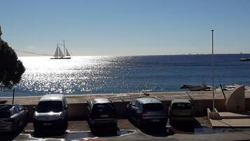 A parking area with cars and a view of the sea and a bridge in the background.