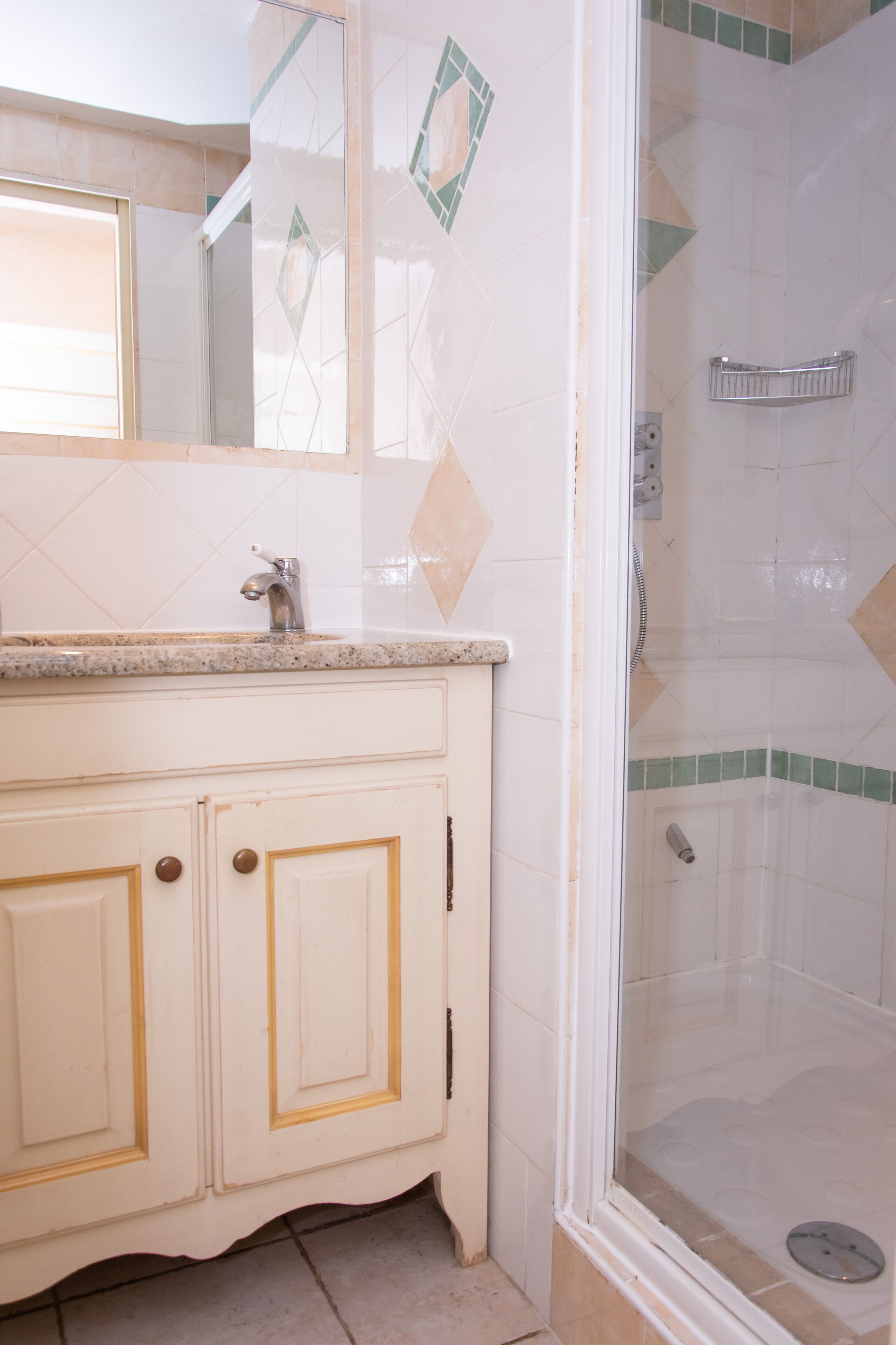 Un baño con tocador blanco, un espejo y zona de ducha con puerta de cristal.