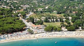 An aerial view of a coastal area with a beach, a road leading to a building, and surrounding greenery. - Hotel & Spa La Villa (Sainte-Maxime)