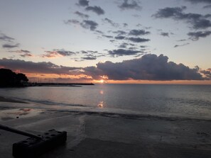 Ein Strand bei Sonnenuntergang, ruhiges Wasser und ein weiter Pier im Hintergrund.