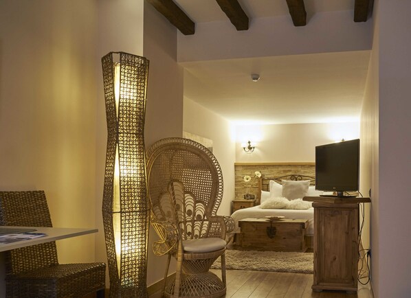 A bedroom with a bed, a television, a wicker chair, a wooden cabinet, and a decorative wall light. - Hotel Rural Casona De Torres (Mondejar)