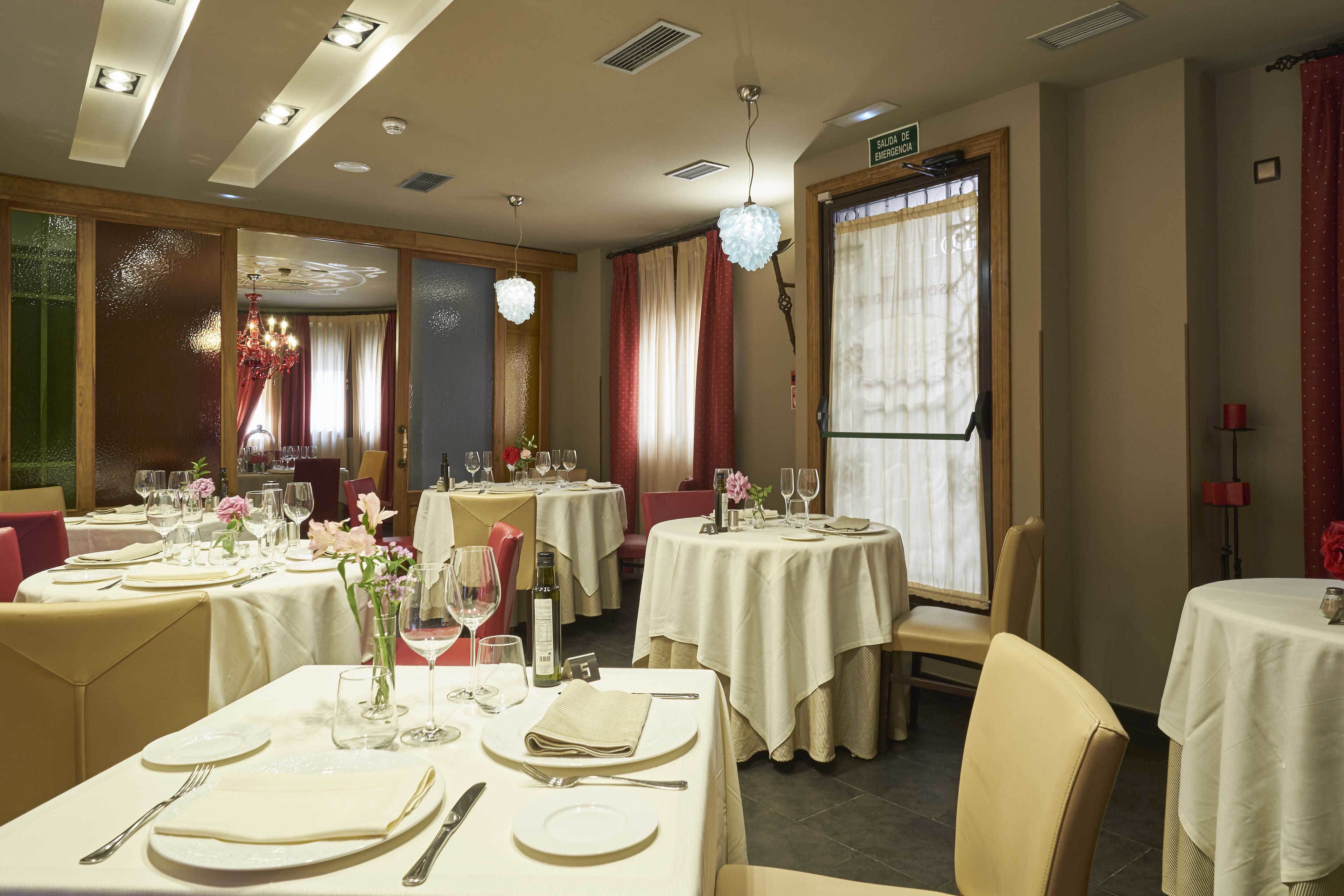 Un comedor con varias mesas redondas dispuestas para comer, cada una con mantel blanco, platos y cubiertos.